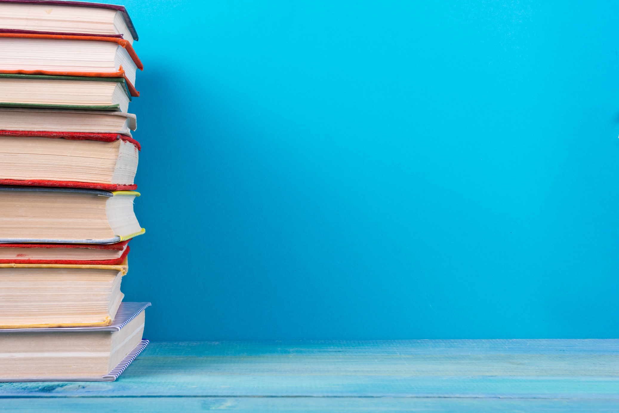 Stack of colorful hardback books, open book on blue background